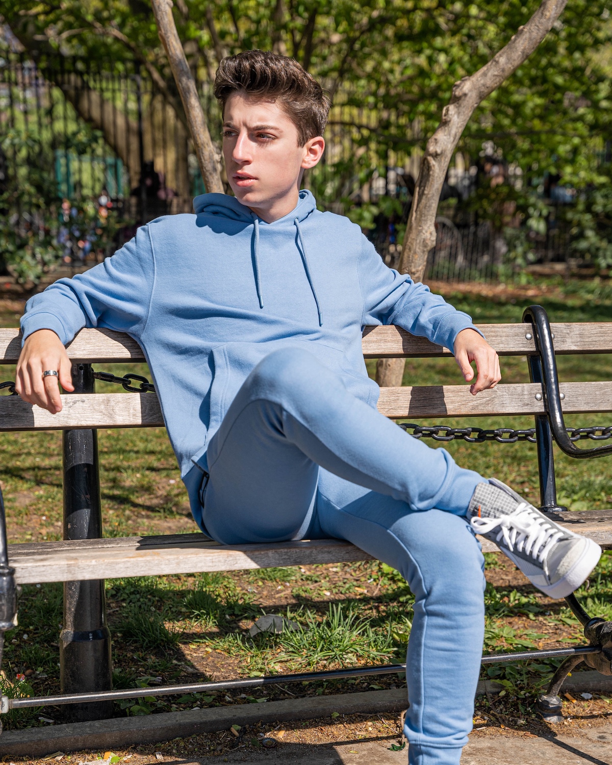 Eitan sits in a blue Topman sweatsuit on a park bench in NYC.