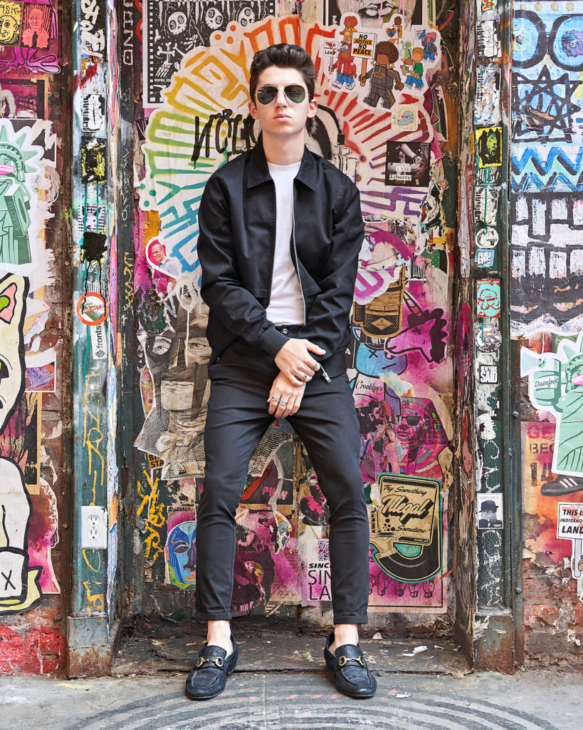 Eitan wears ASOS two-piece black pants and jacket set in frot of NYC Graffiti wall.